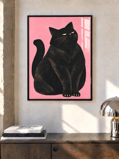 Schwarze Katze vor rosa Hintergrund in einem schwarzen Rahmen an einer sonnigen Wand über einem Holzschrank, neben Büchern und einer Chromlampe.