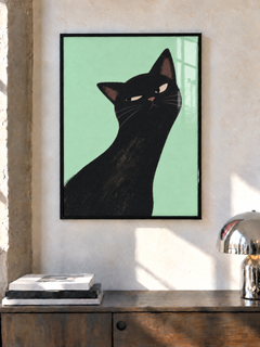 Katzenposter in einem schwarzen Rahmen an einer sonnigen Wand über einer Holzkommode, neben Büchern und einer silbernen Lampe.
