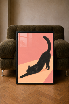 Sunny Stretch black cat art print in a black frame, displayed against a brown armchair